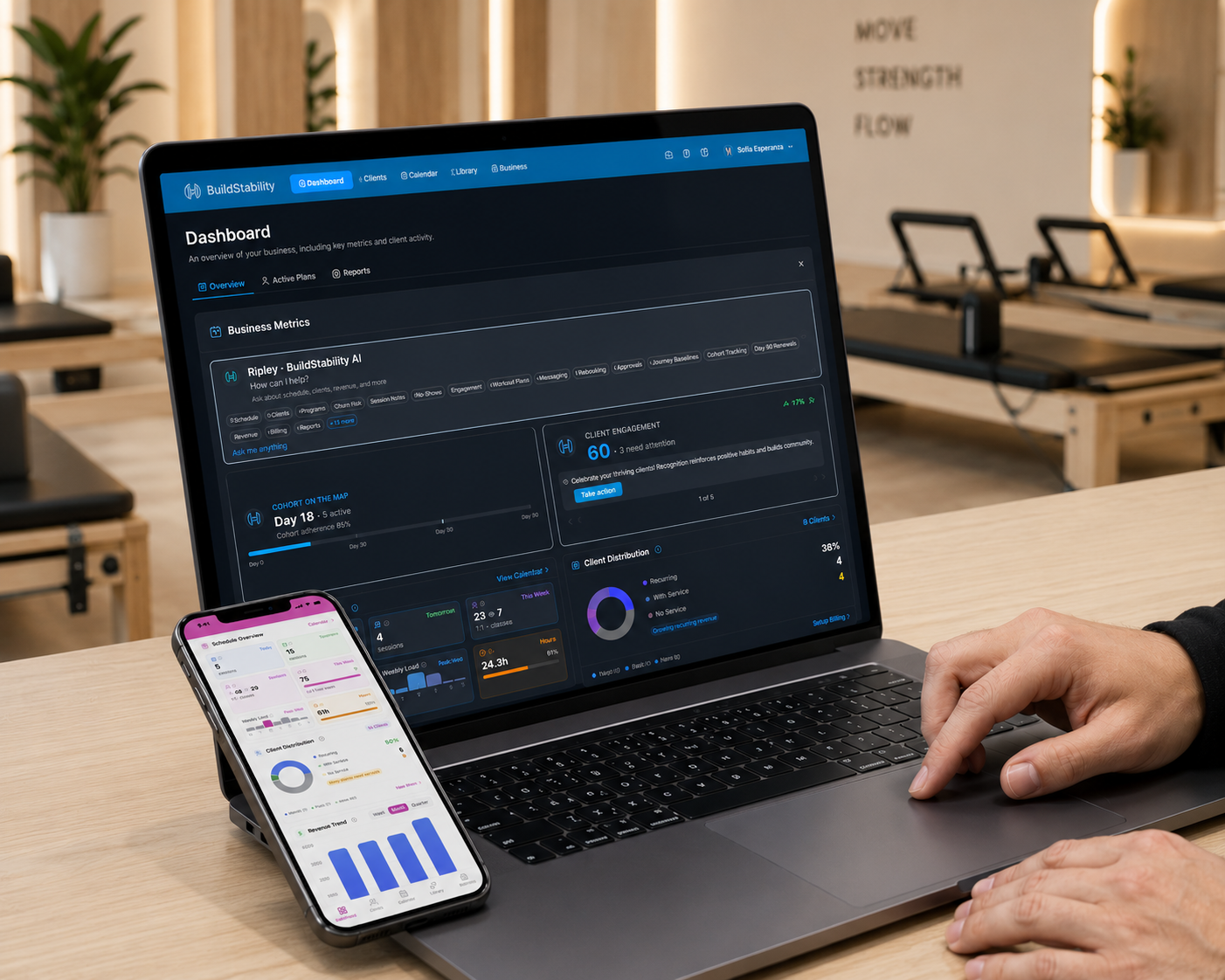 BuildStability dashboard on a MacBook with the studio app open on iPhone, in a premium Pilates reformer studio